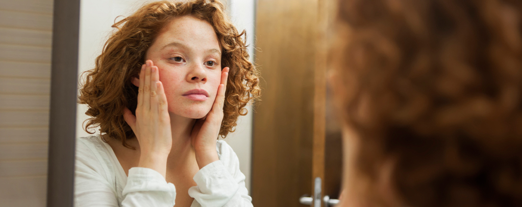Young female adult looking at her face in mirror