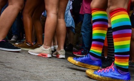 a group of people with only their legs visible, one of the people have rainbow coloured knee-high socks on